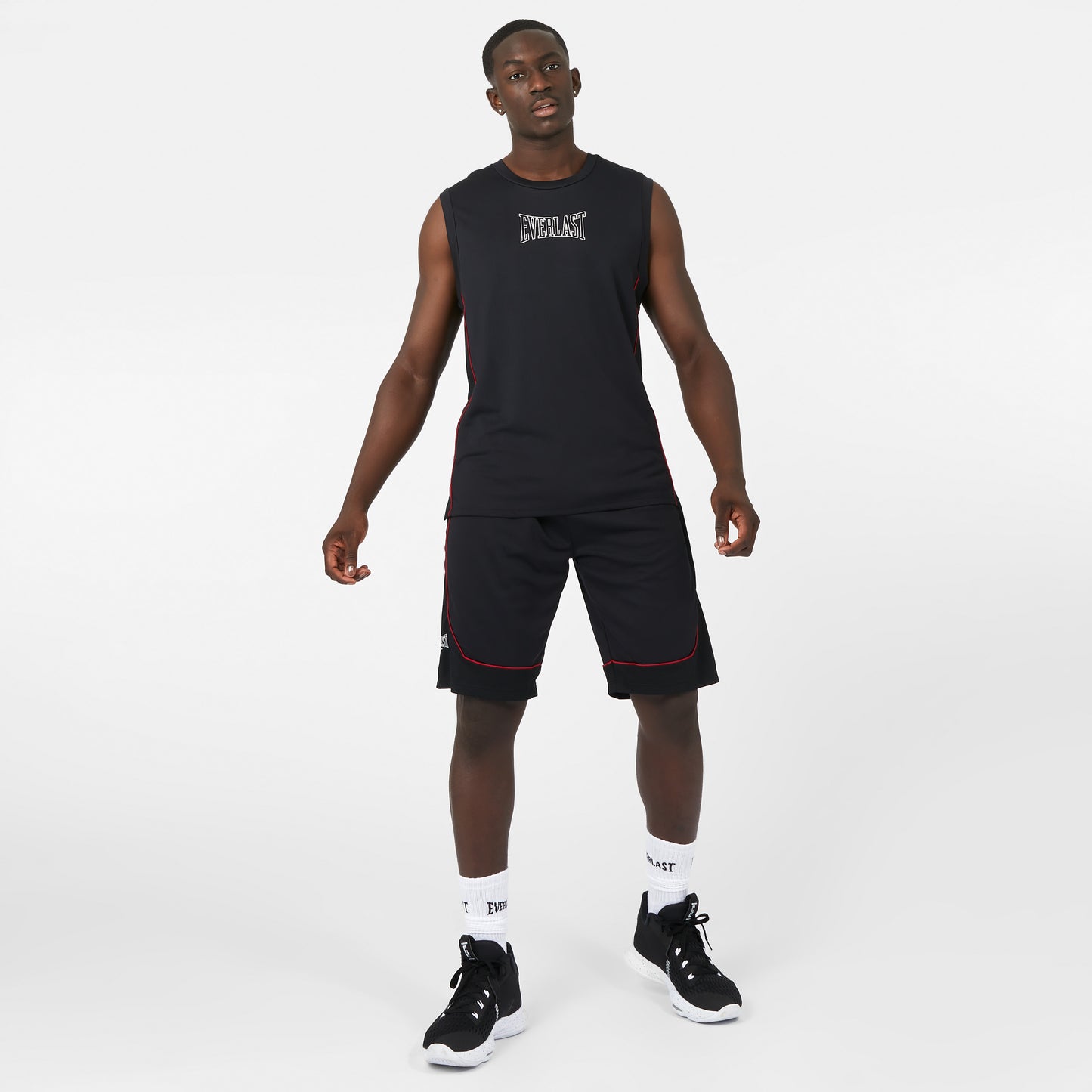 Man wearing a black sleeveless shirt and shorts with white socks and black sneakers on a white background